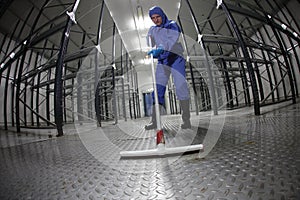 Worker in blue, protective coveralls cleaning floor in empty storehouse