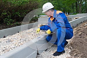 Worker in blue uniform sets the edges of the roadway of a new road