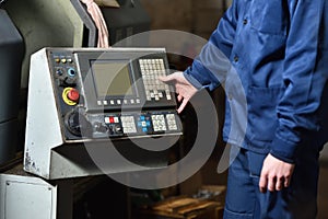 Worker in blue workwear holds hands on the control panel of the CNC machine. Close-up