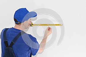 Worker in blue workwear measures the distance using a tape measure