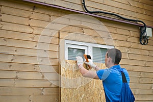 Worker, boarded up the window of the house with a protective shield made of wood, from thieves, when moving to another address