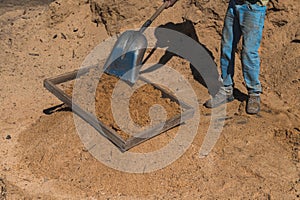 Worker of a brick factory strains sand with a  in a wheelbarrow, for the elaboration of bricks
