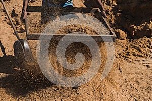 Worker of a brick factory strains sand with a  in a wheelbarrow, for the elaboration of bricks