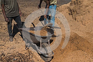 Worker of a brick factory strains sand with a  in a wheelbarrow, for the elaboration of bricks