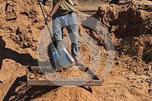 Worker of a brick factory strains sand with a  in a wheelbarrow, for the elaboration of bricks