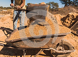 Worker of a brick factory strains sand with a  in a wheelbarrow, for the elaboration of bricks