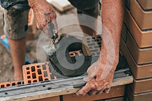 Worker or bricklayer works with trowel laying bricks. Builder makes brickwork on construction site, close up on hands