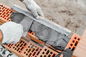 Worker or bricklayer works with trowel laying bricks. Builder makes brickwork on construction site, close up on hands