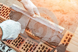 Worker or bricklayer works with trowel laying bricks. Builder makes brickwork on construction site, close up on hands