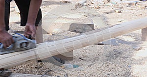 worker buffing the wooden mast of a fishing boat with a the electric sander at a boatyard