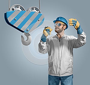 Worker builder in helmet manages the construction process, crane hook