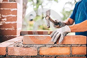 Worker building exterior walls, using hammer for laying bricks in cement. Detail of worker with tools