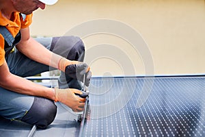 Worker building photovoltaic solar panel system on rooftop of house with help of hex key.