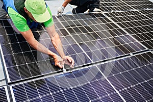Worker building photovoltaic solar panel system on rooftop of house with help of wrench.