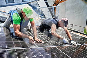 Worker building photovoltaic solar panel system on rooftop of house with help of wrench.