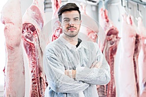 Worker in butchery standing in front of carcasses