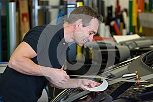 Worker in car wrapping workshop glues foil to car