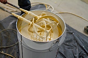 The worker is carefully mixing epoxy composites in a metal bucket to create high-quality polyurethane resin. This process requires