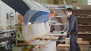 Worker carpenter handles wooden furniture parts on the machine on the factory