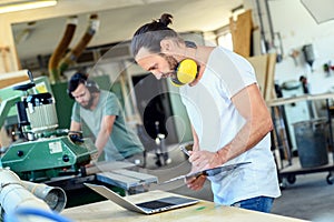Worker in a carpenter`s workshop with computer and clipboard