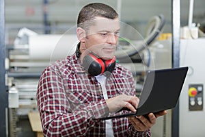 worker in carpenters workshop with clipboard and computer