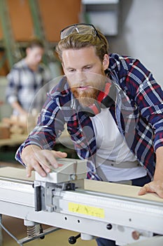 Worker in carpenters workshop using saw machine