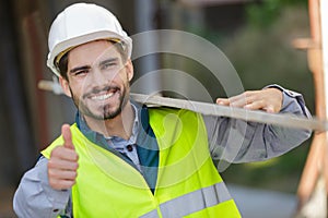 worker at carpentry shop smiling and carrying wood