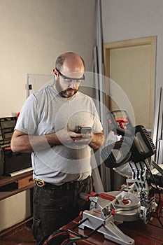 Worker in carpentry workshop sending a message by smart phone