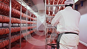 Worker carrying rack with delicious fresh sausage bunches along production plant storage room.