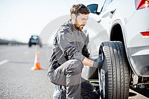 Worker changing car wheel on the highway