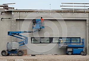 A worker on a cherry picker finishes the newly constructed facade of a new building. On the right an aerial platform