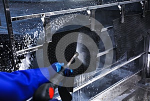 Worker cleaning automobile floor mat with high pressure water jet at car wash, closeup