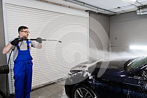 Worker cleaning automobile with high pressure water jet at car wash.