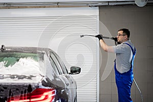 Worker cleaning automobile with high pressure water jet at car wash.