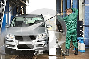 Worker cleaning car with pressured water