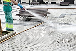 Worker cleaning a city square with water using a hosepipe