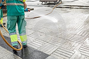 Worker cleaning a city square with water using a hosepipe