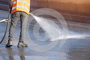 Worker cleaning driveway with gasoline high pressure washer splashing the dirt, asphalt road. High pressure cleaning