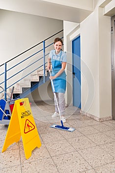 Worker With Cleaning Equipments And Wet Floor Sign