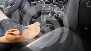 Worker is cleaning handle of gearbox and control panel inside automobile in a car washing service