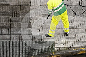 Worker cleaning the street sidewalk with high pressure water jet