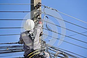 A worker climbs an electric pole to fix a broken wire wearing full safety harness.