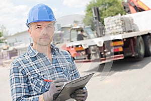 Worker with clipboard in front truck