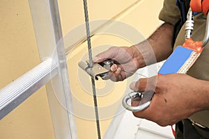 Worker clipping industrial Karabiner connected with fall arrest shock absorbing safety lanyard device into vertical lifeline