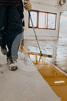 Worker, coating floor with self-leveling epoxy resin in industrial deposit