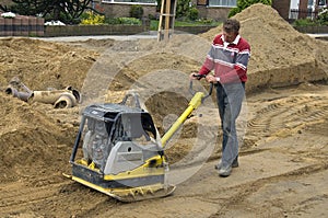 Worker compacting sand with vibrating plate tamper