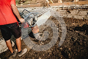 worker compacting soil with vibration compaction machine during foundation works