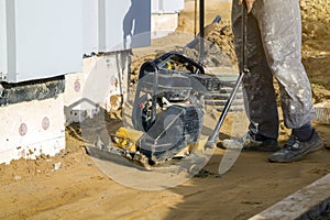 worker compresses sand in blind area around building with special working tool & x28;tamping machine or vibratory plate