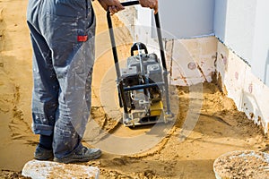 worker compresses sand in blind area around building with special working tool & x28;tamping machine or vibratory plate
