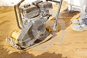 worker compresses sand in blind area around building with special working tool & x28;tamping machine